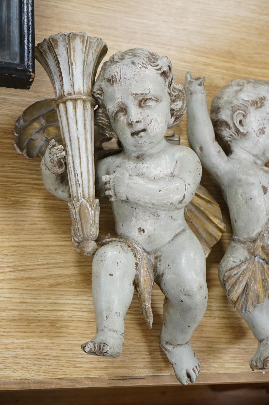 A pair of cream painted and parcel gilt carved wood putti candleholders, 32cm high